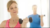 Mature woman lifting dumbbell with man in background at home