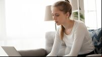 Young woman freelancer using laptop working online making notes