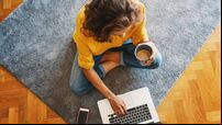 young girl woman in a yellow shirt works on a laptop with a mug of coffee at home in the living room on the carpet, remote work