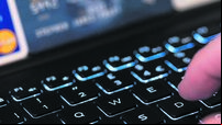 A hand typing on a keyboard with a computer screen and credit cards in the background. Concept: fraud using stolen credit cards