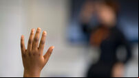 A young black child puts his hand up when asked a question in a school classroom in Wales, UK.