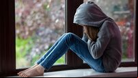 Sad girl in hooded top, sitting on a window ledge with head in hands in despair