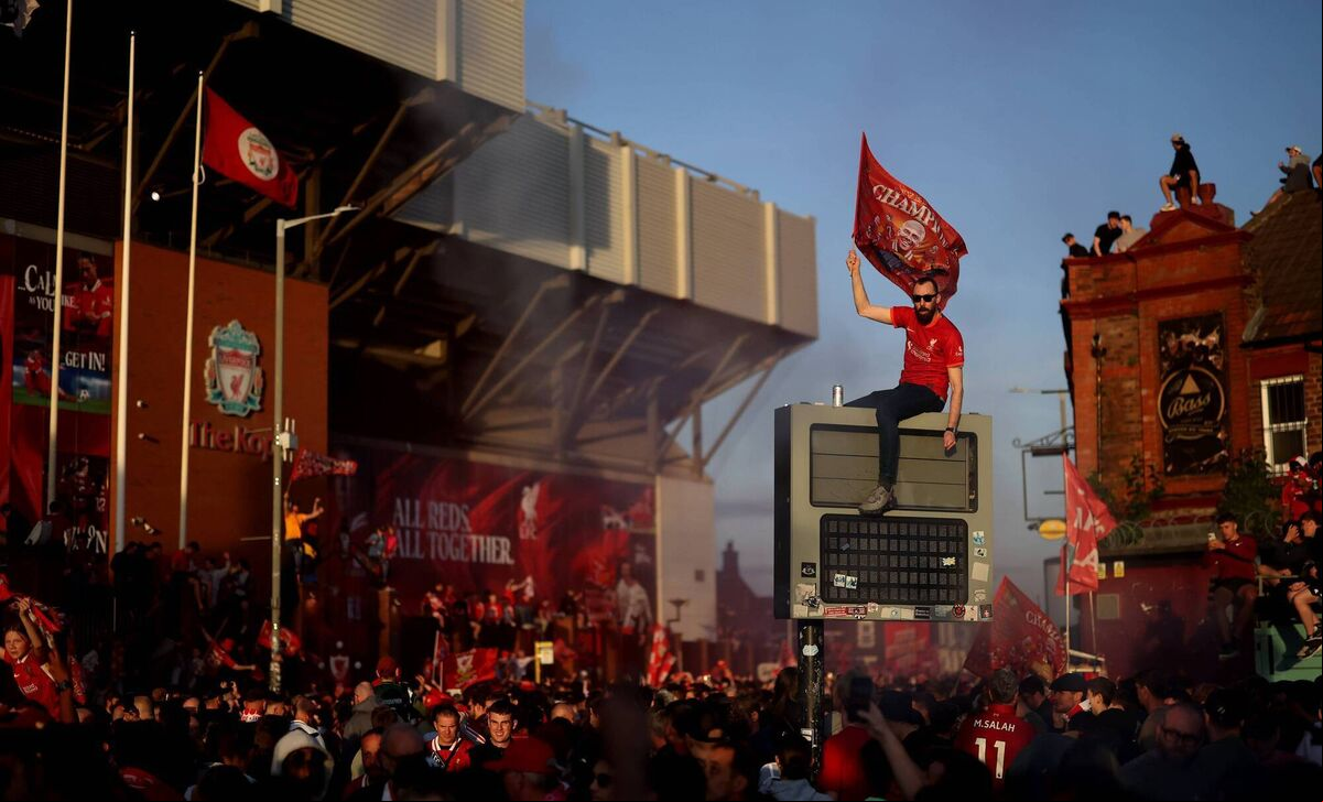 A fan of Liverpool waves a flag, while sitting on top of a sign, as they celebrate the teams victory and confirmation of winning the Premier League title, outside Anfield. Picture: Carl Recine/Getty Images A fan of Liverpool waves a flag, while sitting on top of a sign, as they celebrate the teams victory and confirmation of winning the Premier League title, outside Anfield. Picture: Carl Recine/Getty Images