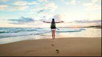 Woman backpacker greeting a sunset at the ocean coast