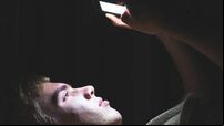 Depressed teenager on his phone in the dark.